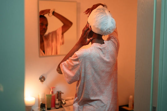 Woman applying towel to hair in bathroom mirror.